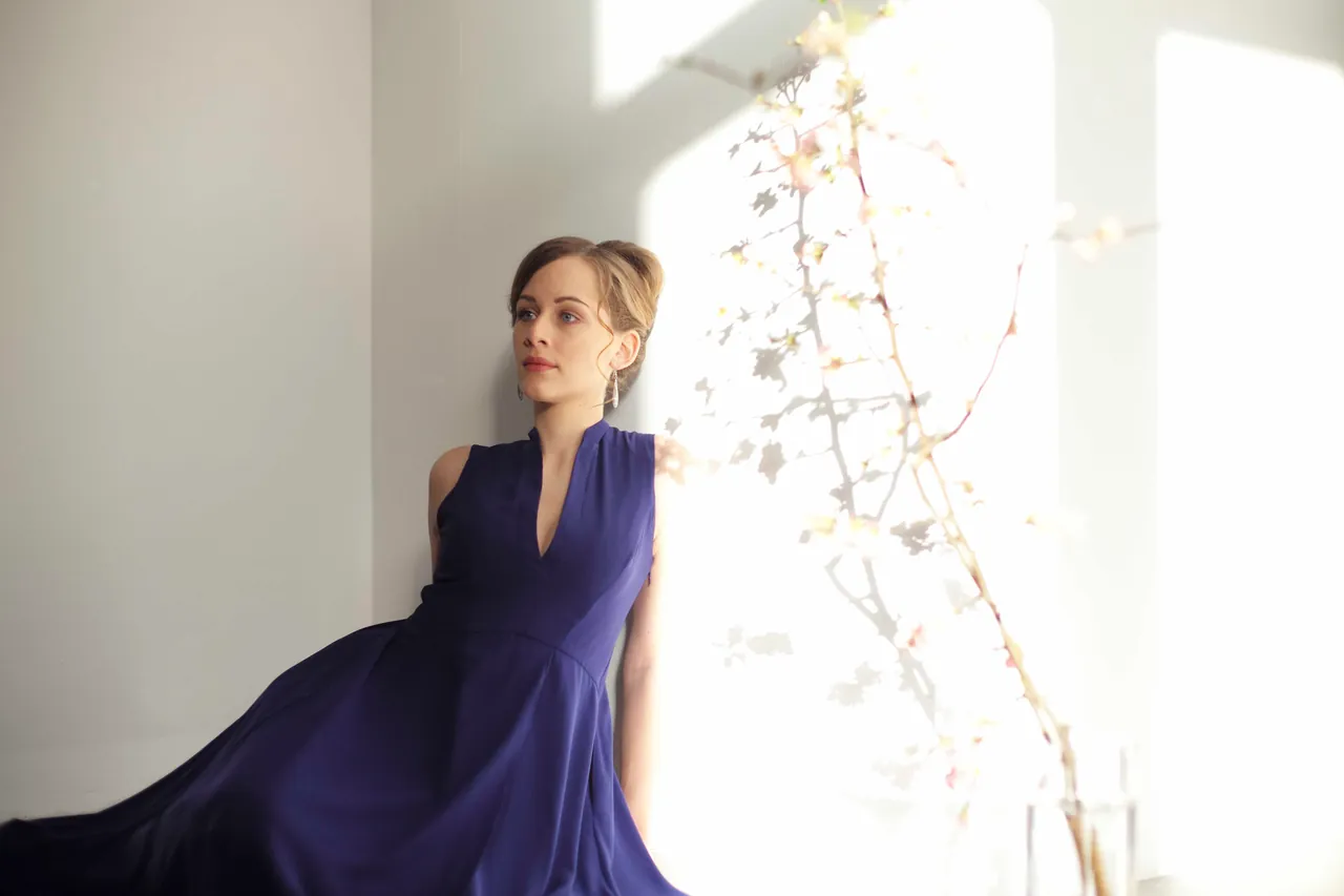 Anna Lucia Richter con un vestido azul junto a una ventana luminosa