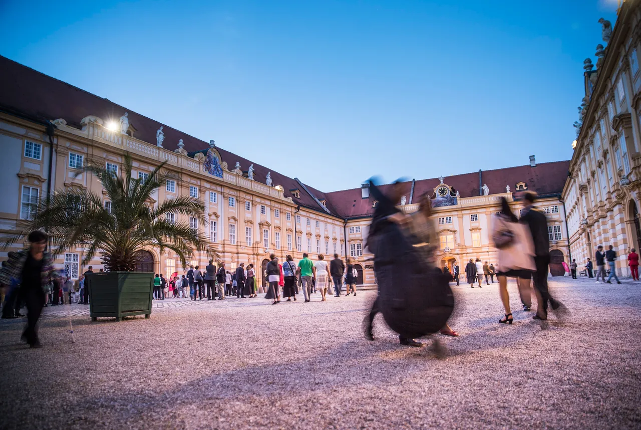 Mitwirkende eilen in der Abenddämmerung über einen Innenhof des Stiftes Melk