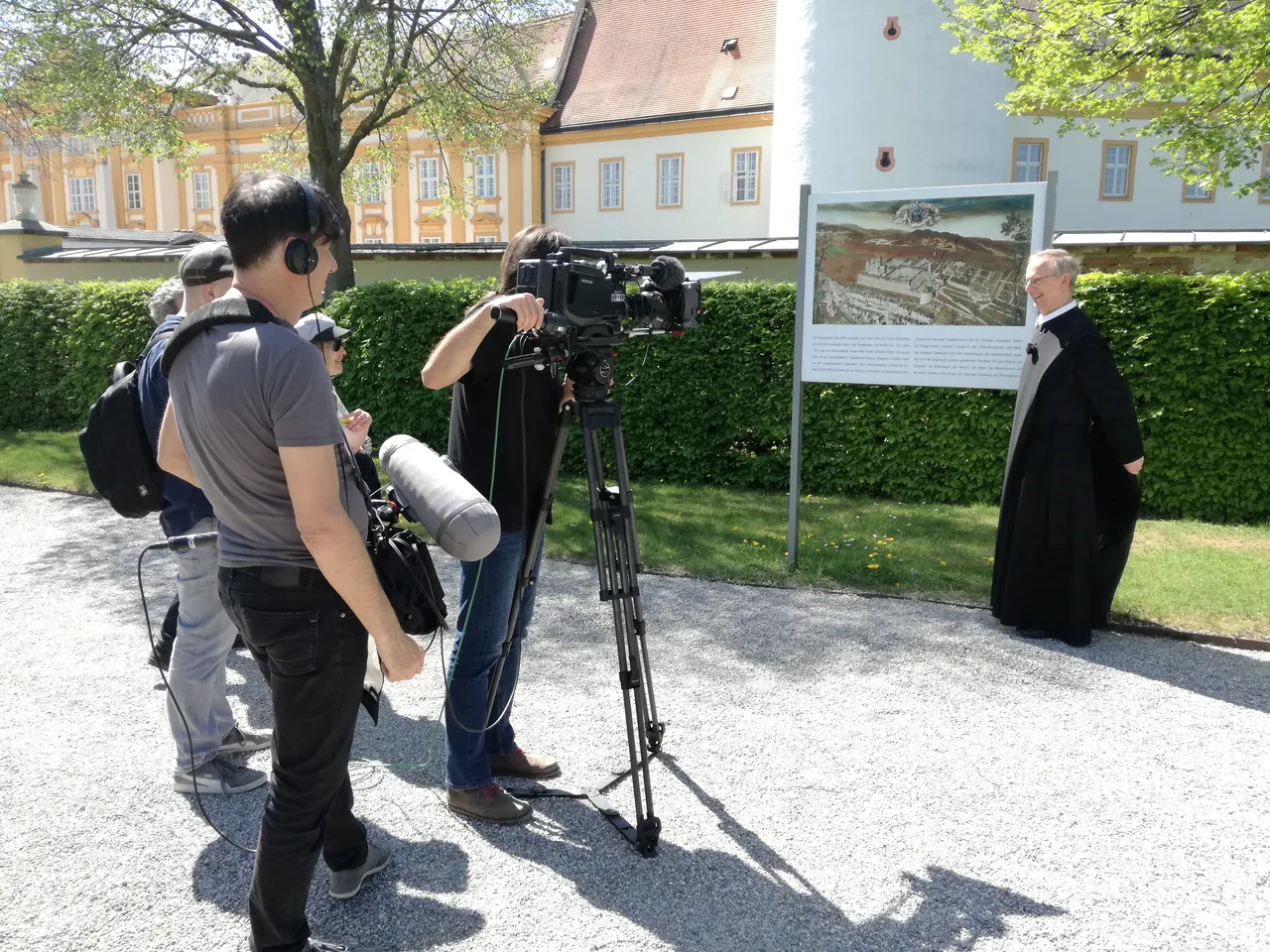 Dreharbeiten im Stiftspark: Pater Martin Rotheneder vor einer Schautafel mit dem Plan der Klosteranlage