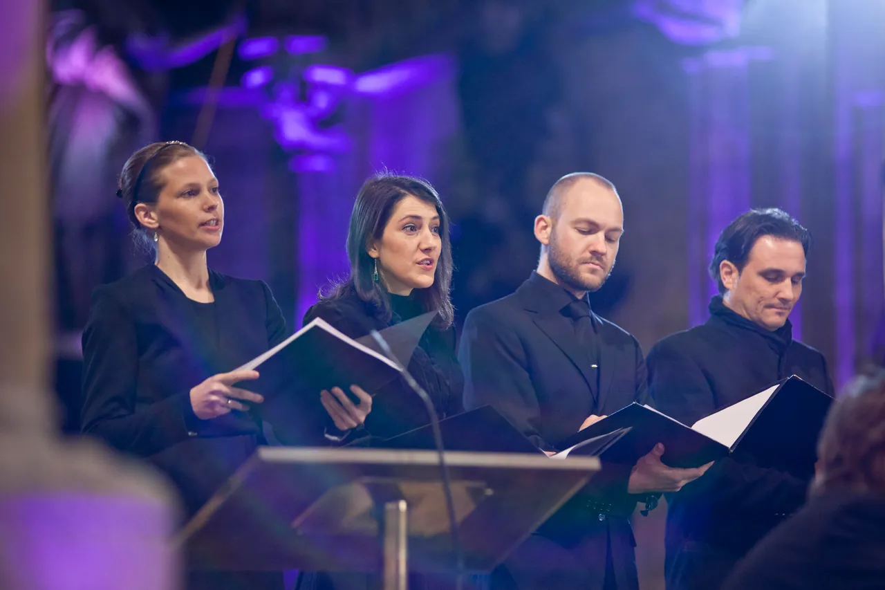 Four singers with their scores in front of purple-lit pillars