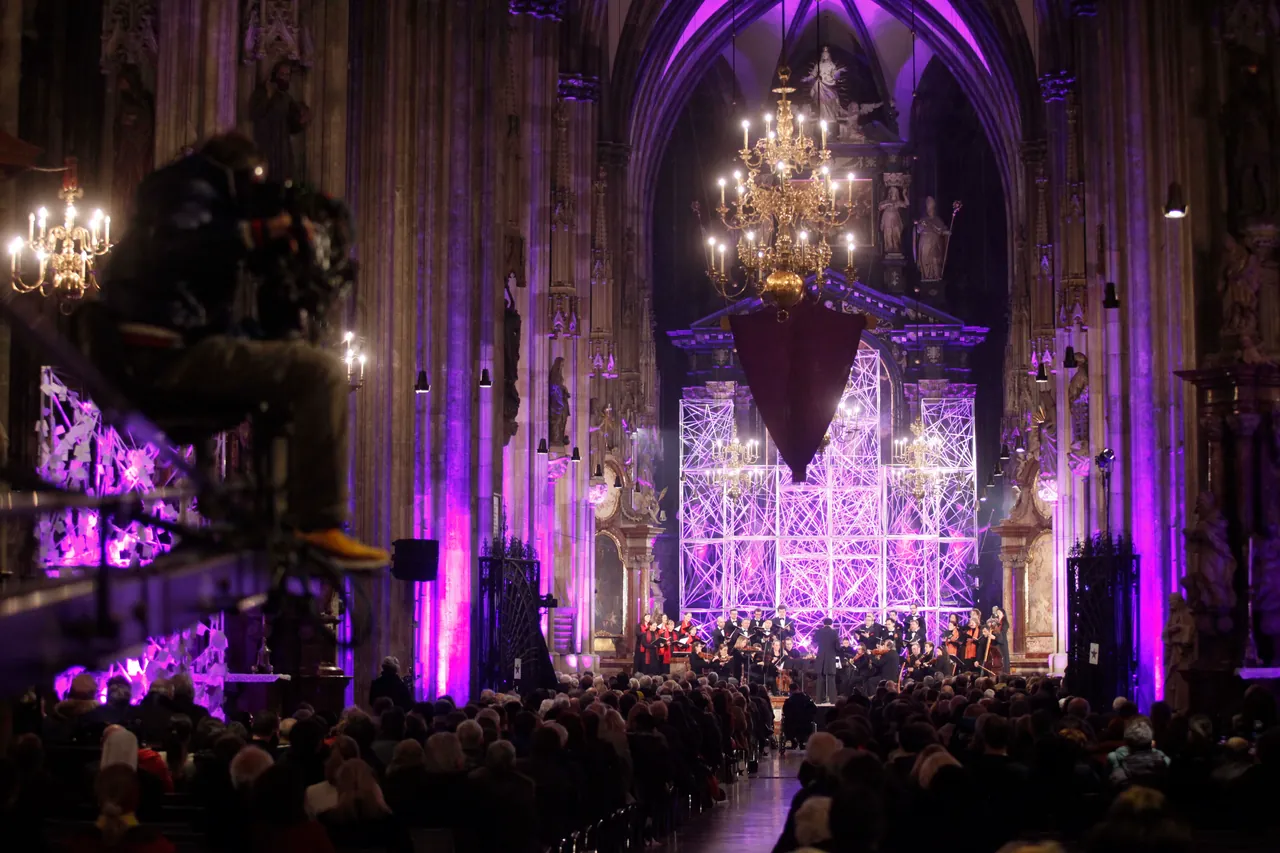 View down the purple-lit nave of St. Stephen’s Cathedral to the choir and orchestra before the high altar, with a camera operator on the left