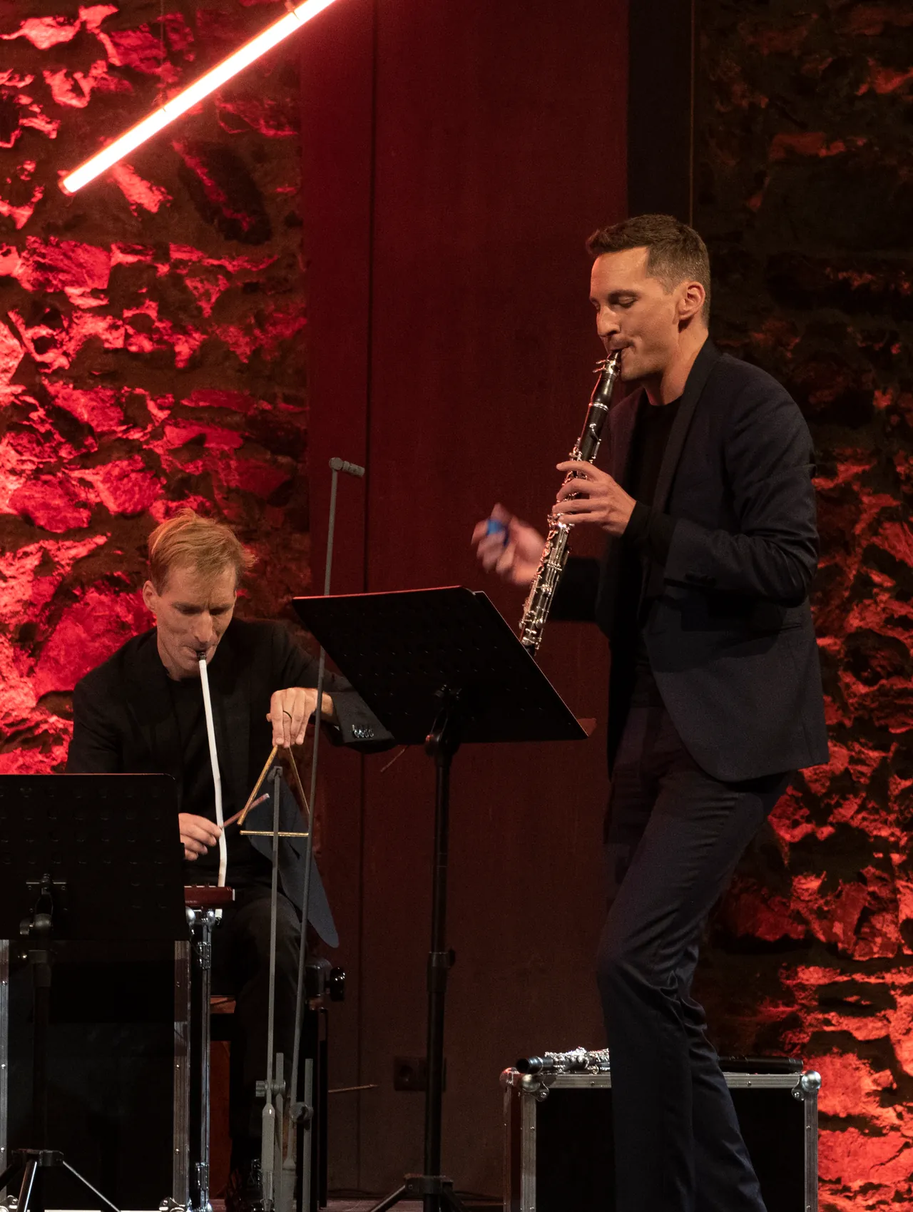 Daniel Ottensamer al clarinete, junto a otro miembro del conjunto, ante el muro de piedra iluminado en rojo