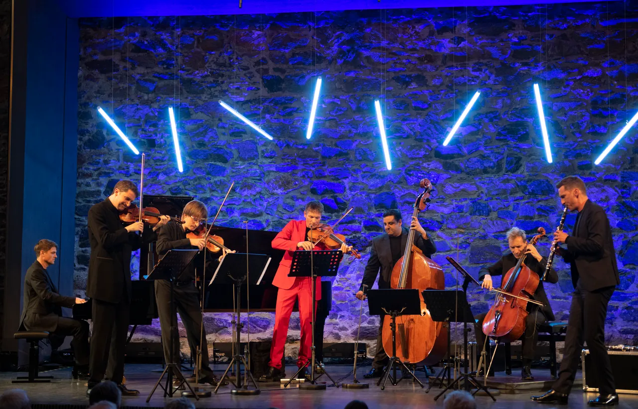 Philharmonix en el escenario del castillo de Taggenbrunn, ante el muro de piedra iluminado en azul y bajo barras de luz
