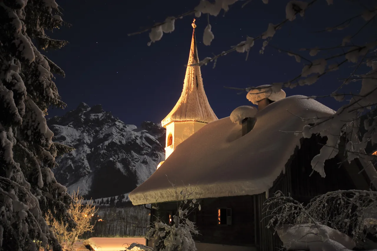 Die Wallfahrtskirche von Werfenweng in einer verschneiten Winternacht, dahinter die Berge
