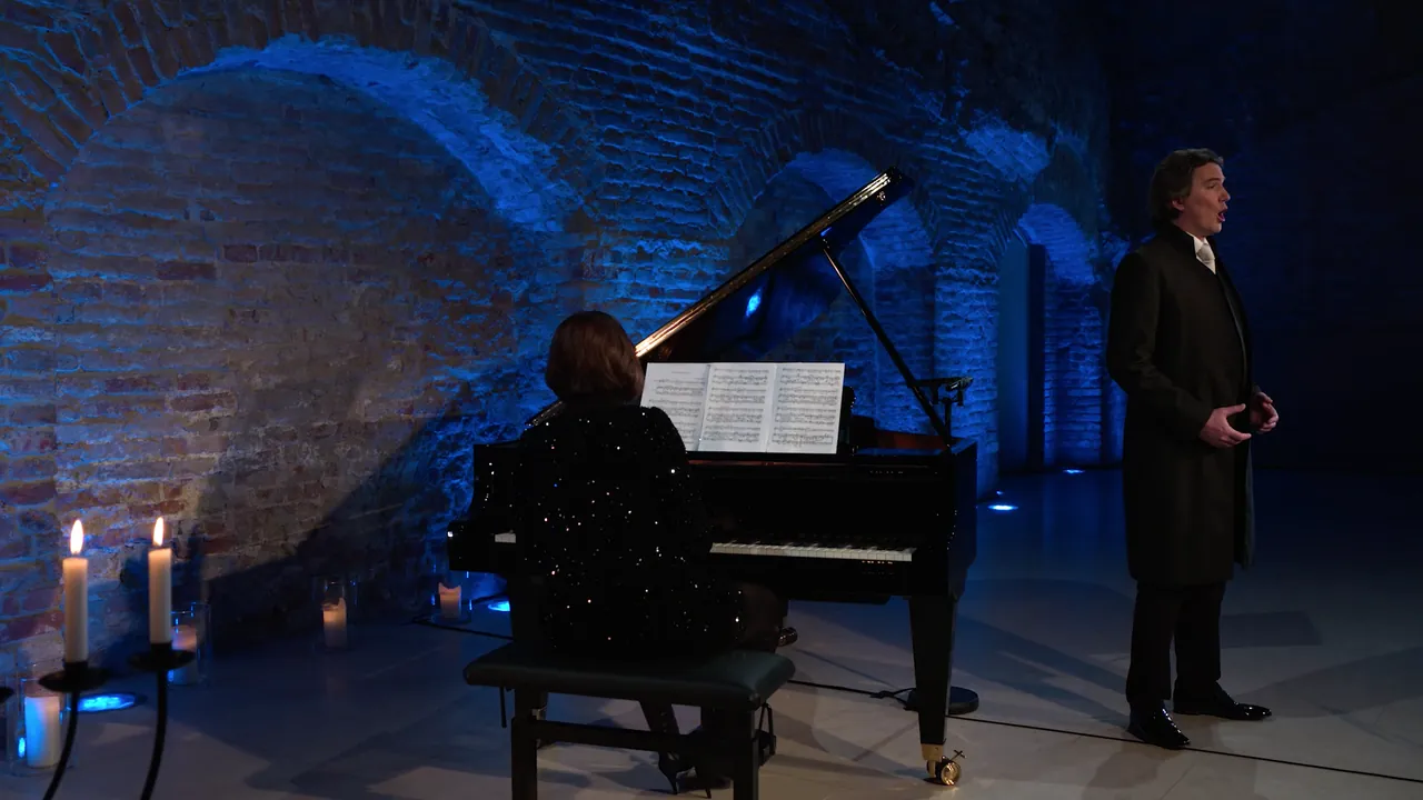 Günter Haumer singt, begleitet von Magda Amara am Flügel, im blau beleuchteten Gewölbe
